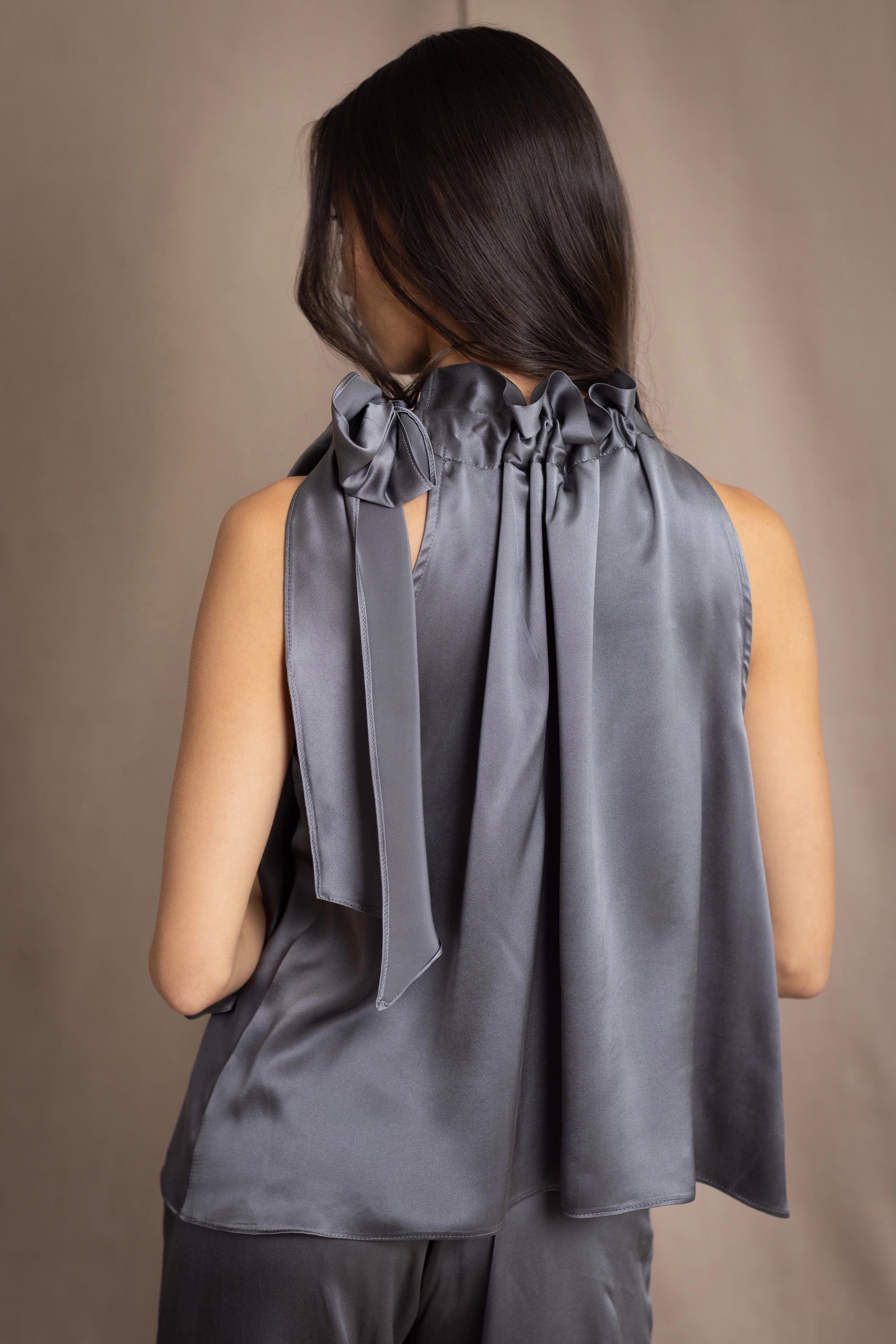 Woman wearing a dark gray sleeveless silk blouse with a bow and halter neck detail