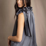 Woman wearing a dark gray sleeveless silk blouse with a bow and halter neck
