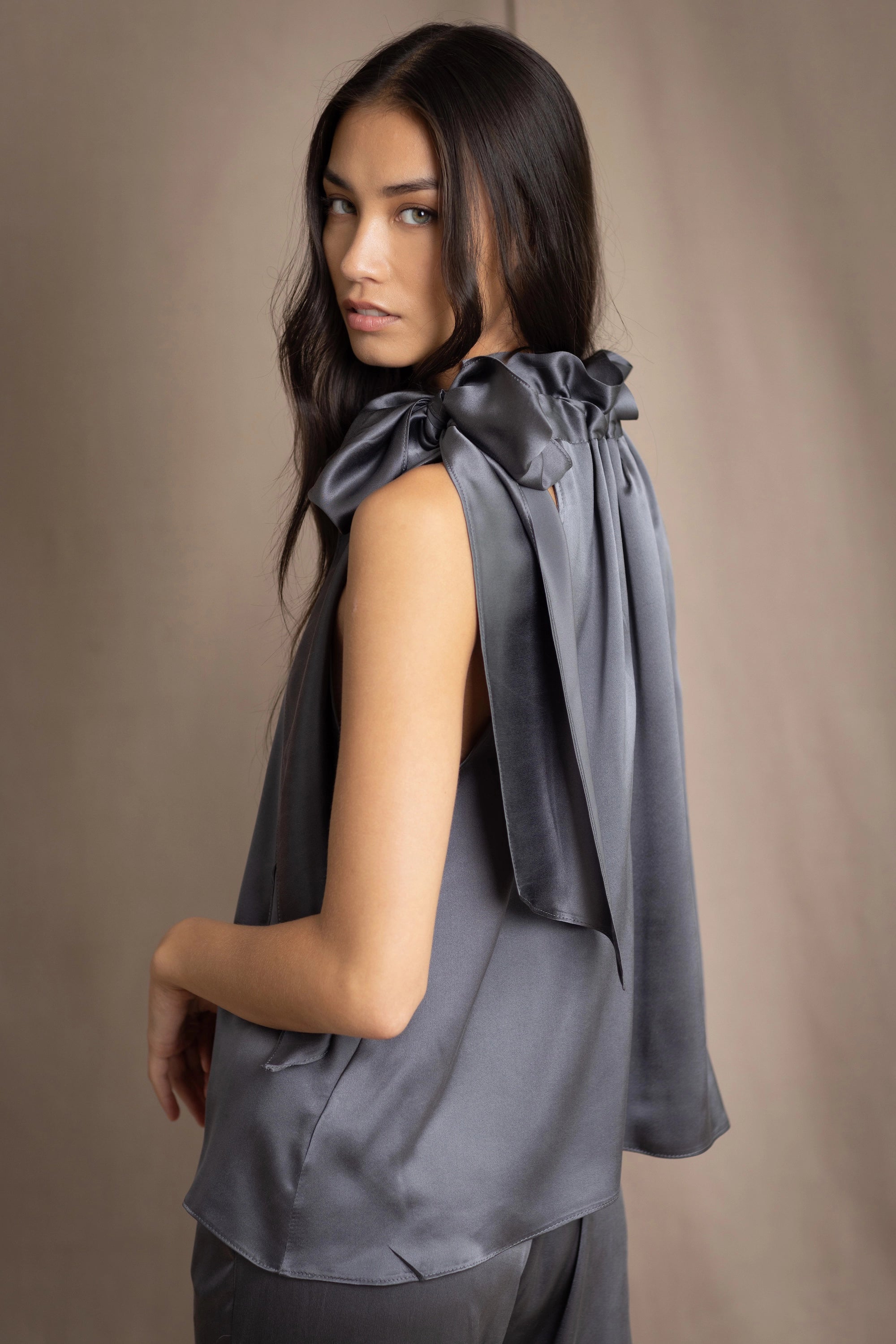 Woman wearing a dark gray sleeveless silk blouse with a bow and halter neck