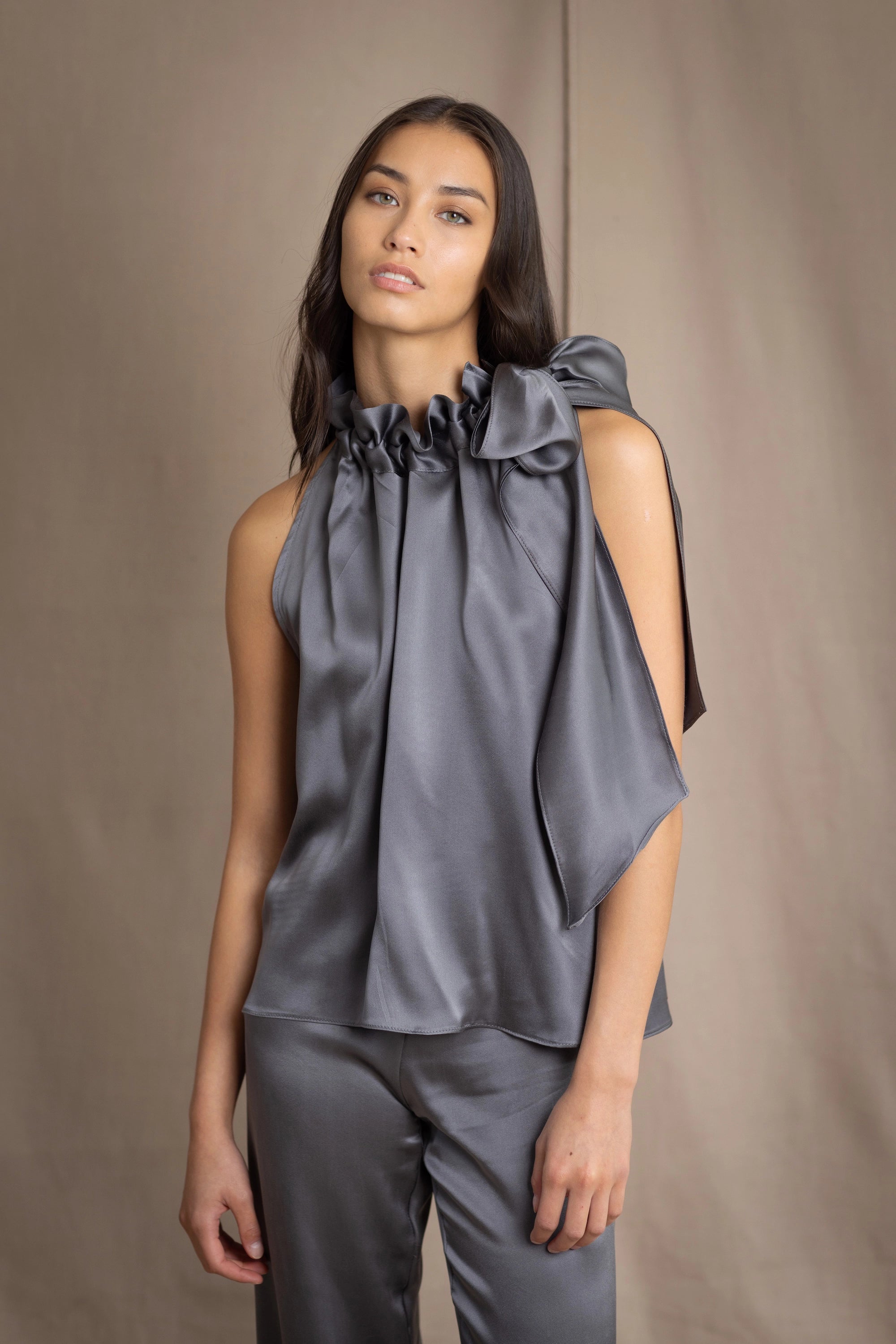 Woman wearing a dark gray sleeveless silk blouse with a bow and halter neck with matching trousers