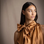 Woman wearing a bronze sleeveless silk pussy bow top with a large bow