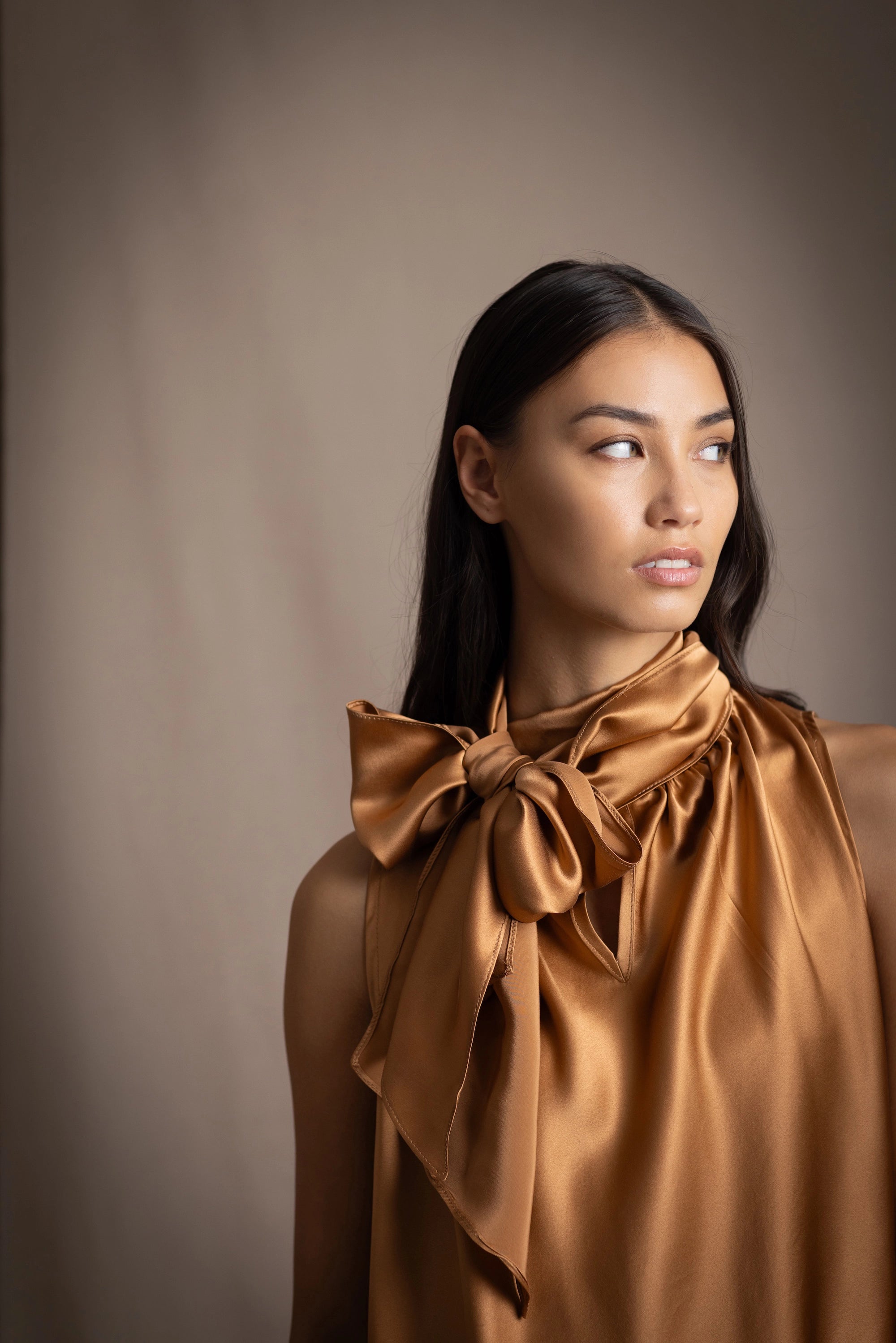 Woman wearing a bronze sleeveless silk pussy bow top with a large bow