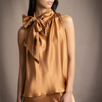 Woman wearing a bronze sleeveless silk pussy bow top with a large bow and matching pants
