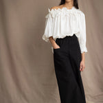 Woman wearing a white silk blouse with ruffled details and black trousers