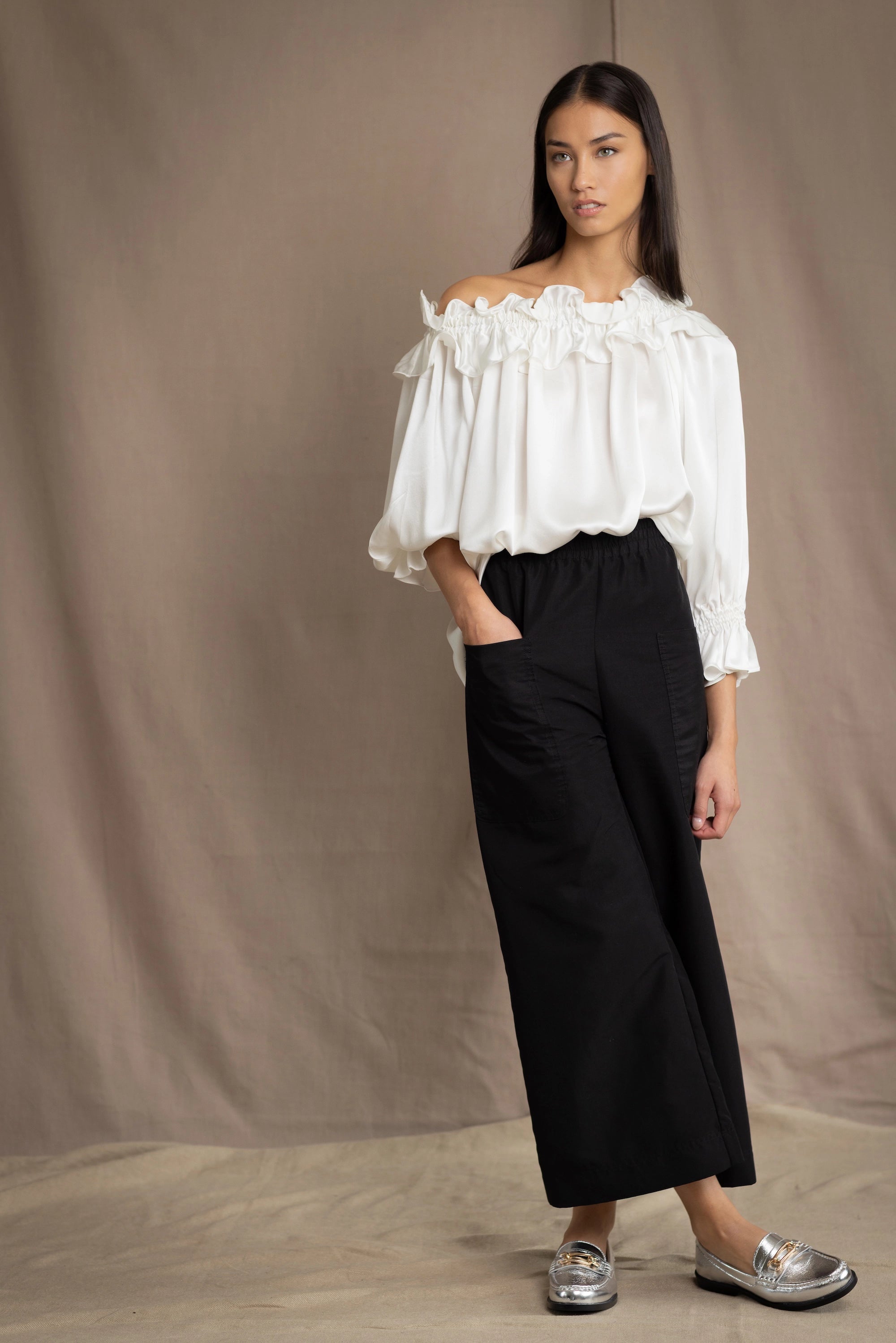 Woman wearing a white silk blouse with ruffled details and black trousers