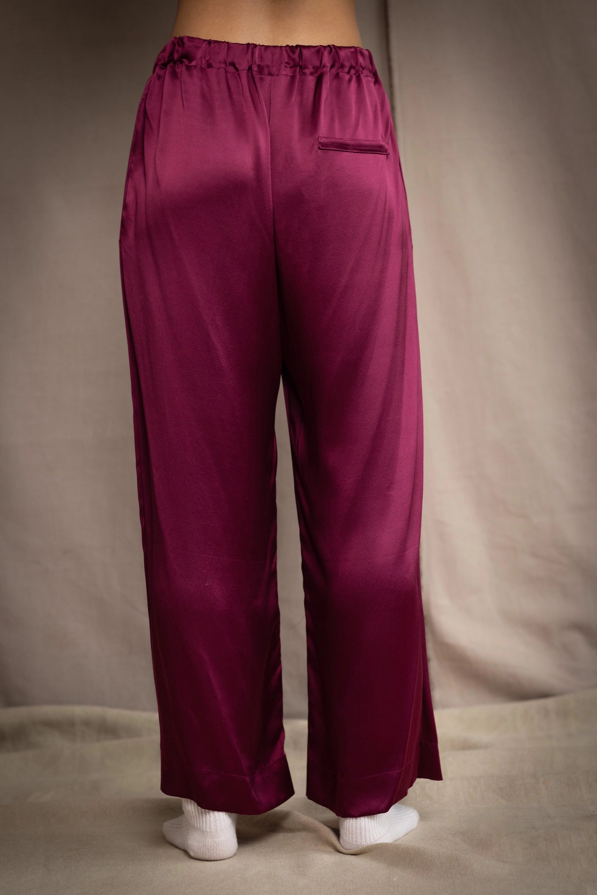 a woman wears burgundy silk trousers with elastic waist