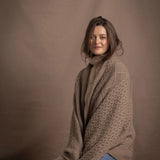 A lady wears a pure cashmere aran blanket in taupe over a beige aran sweater