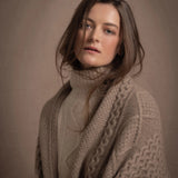 A lady wears a pure cashmere aran blanket in taupe over a beige aran sweater