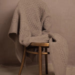 A pure 100% cashmere aran blanket in taupe over a chair