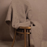 A pure 100% cashmere aran blanket in taupe over a chair