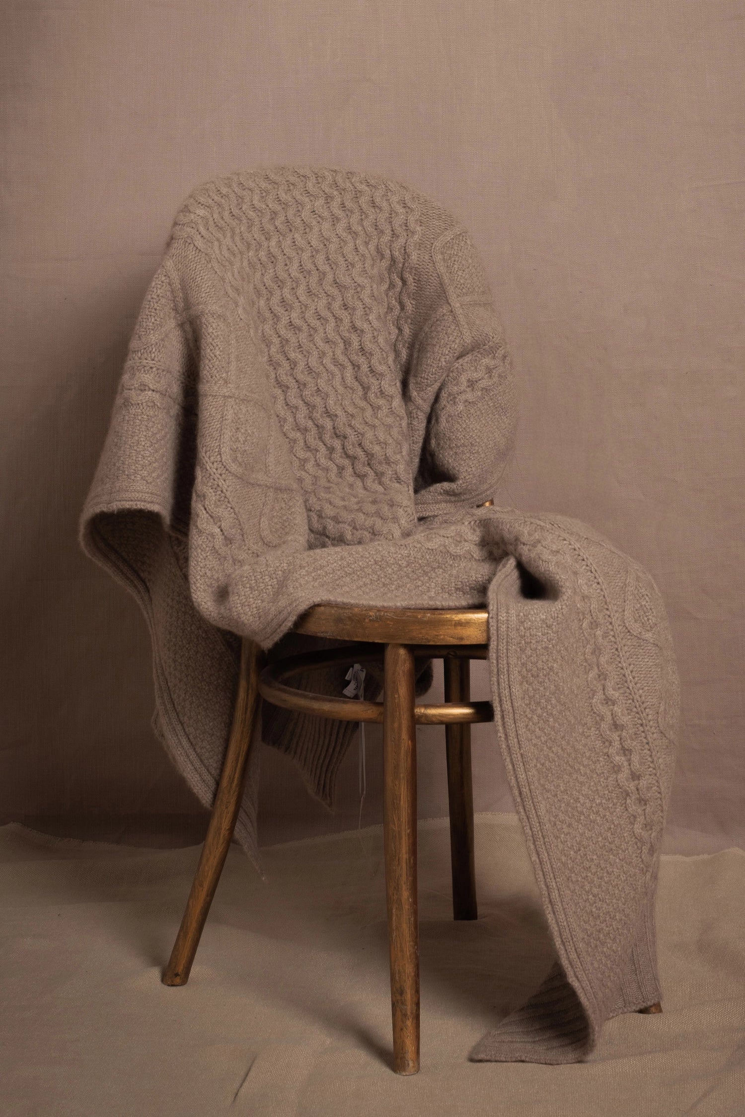 A pure 100% cashmere aran blanket in taupe over a chair