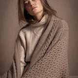 A lady wears a pure cashmere aran blanket in taupe over a beige aran sweater