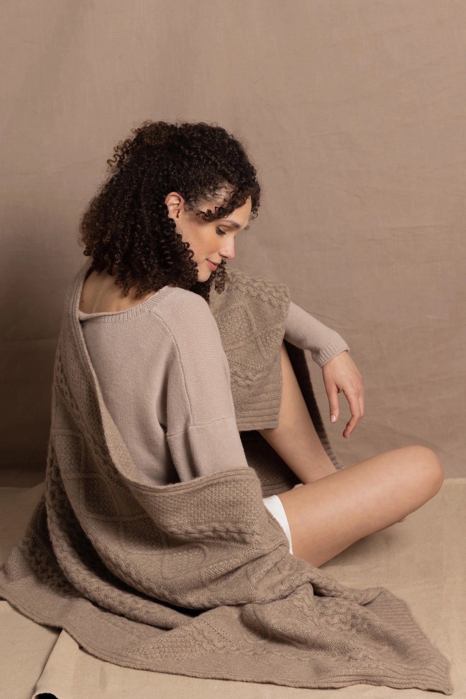 A lady wears a pure cashmere aran blanket in taupe over a beige cashmere sweater