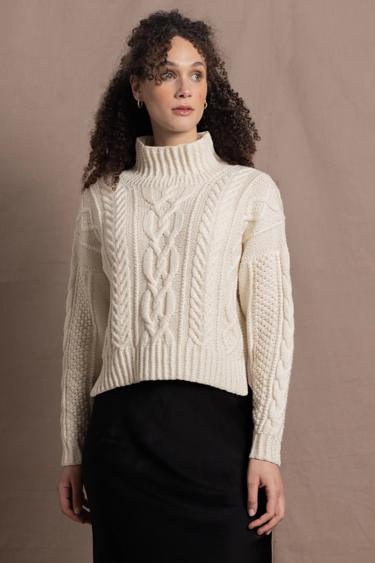 A woman wears a traditional Irish Aran Sweater made in 100% Cashmere over a black silk skirt