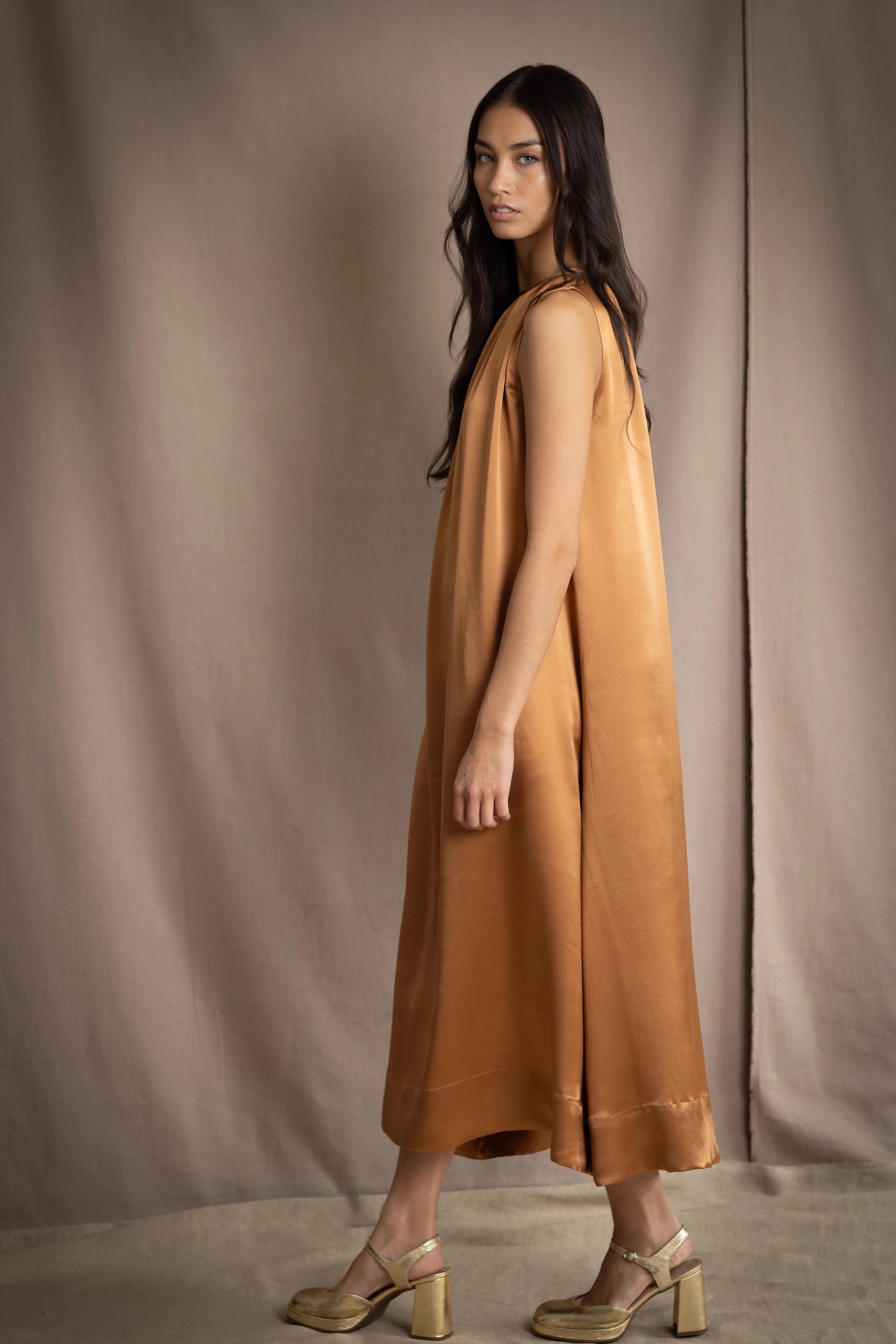 a woman wearing a bronze silk sleeveless dress
