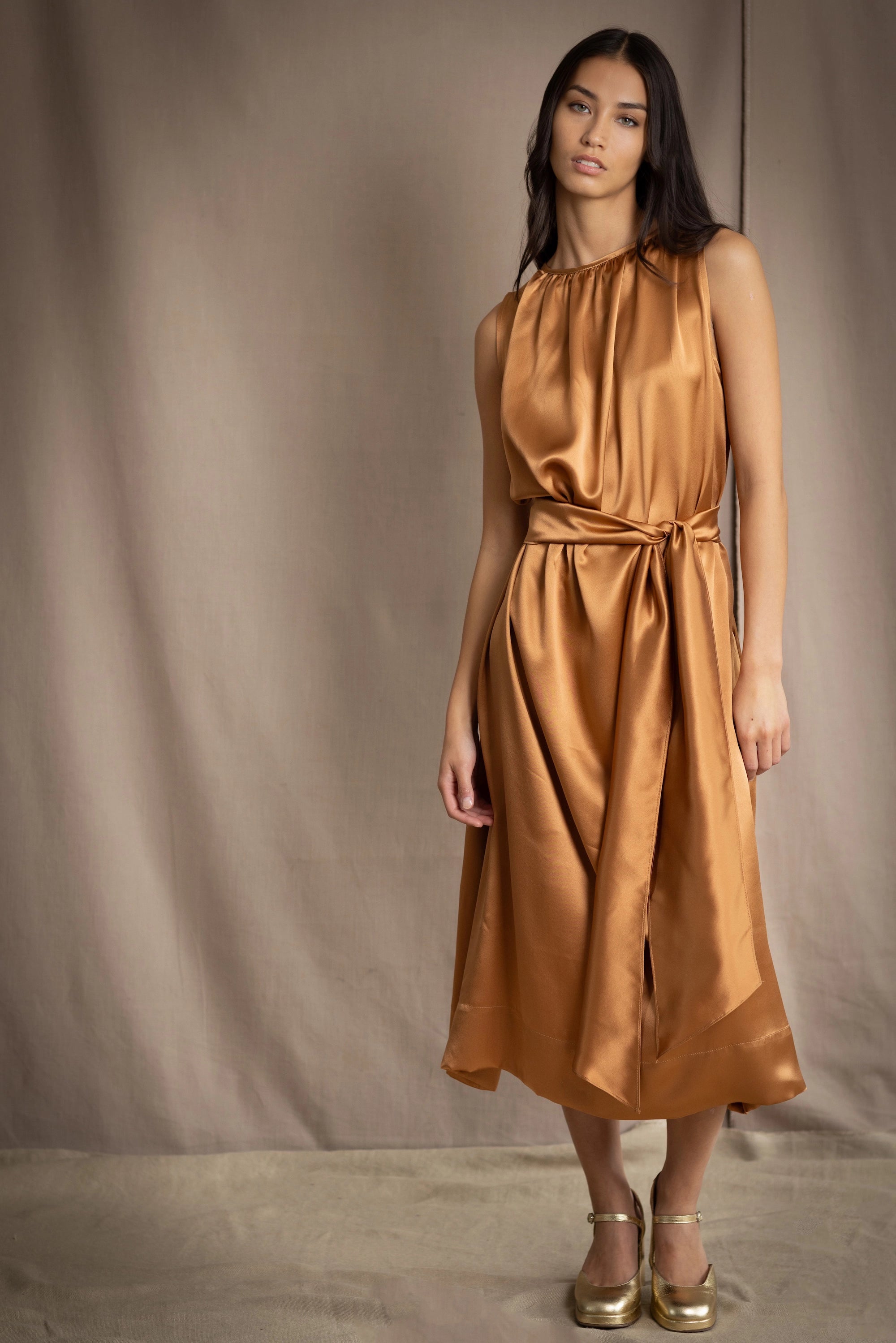 a woman wearing a bronze silk sleeveless dress