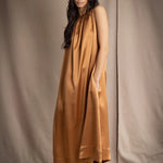 a woman wearing a bronze silk sleeveless dress
