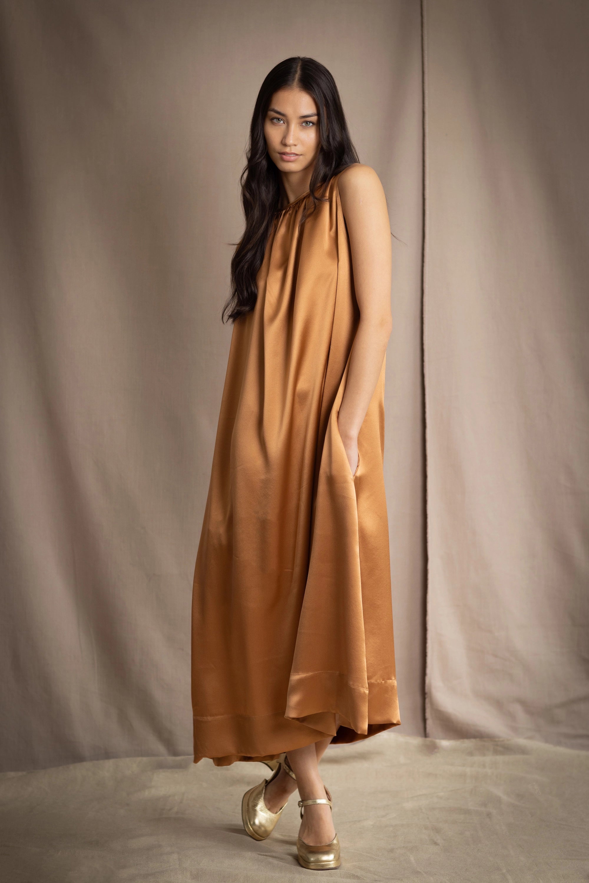 a woman wearing a bronze silk sleeveless dress