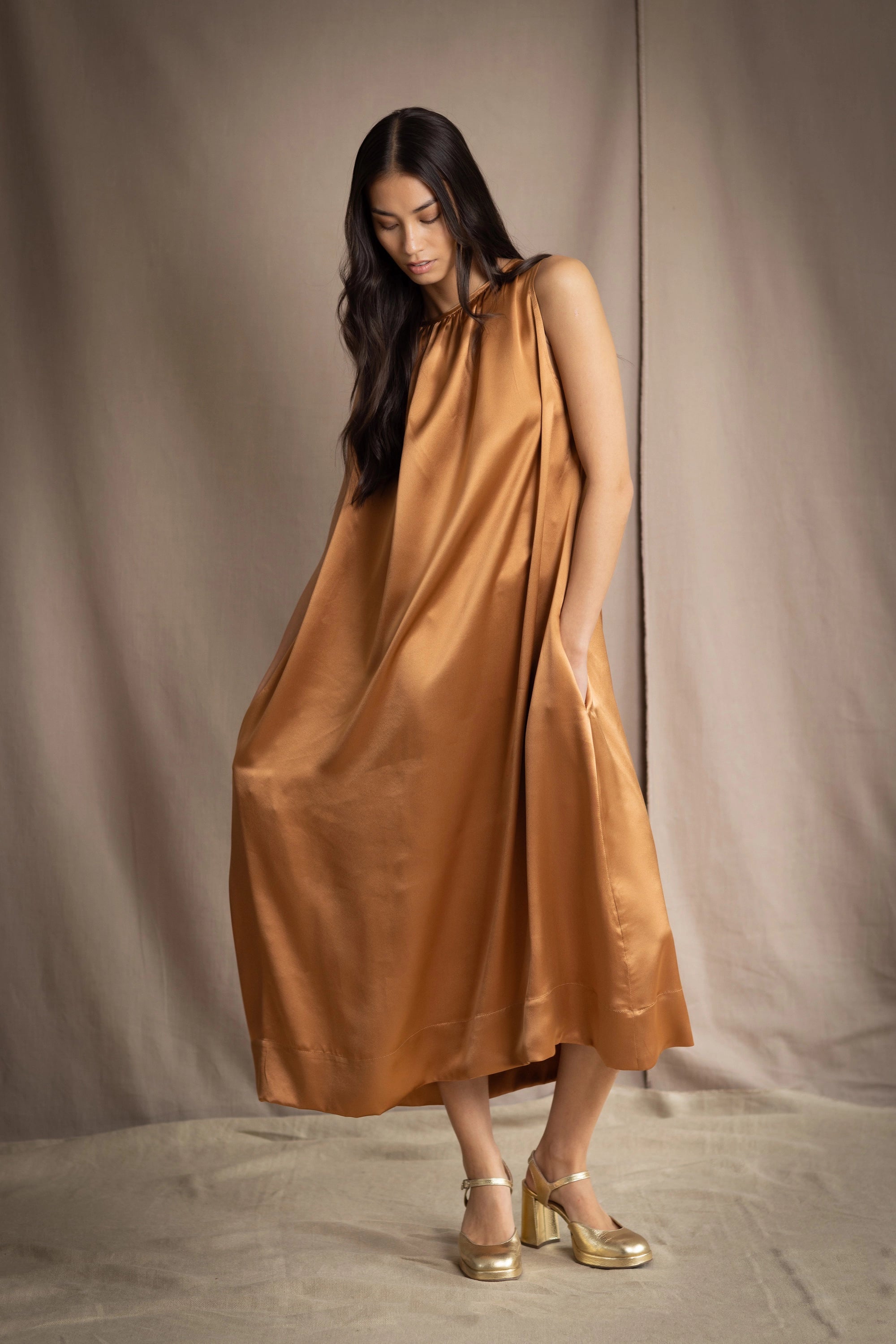 a woman wearing a bronze silk sleeveless dress