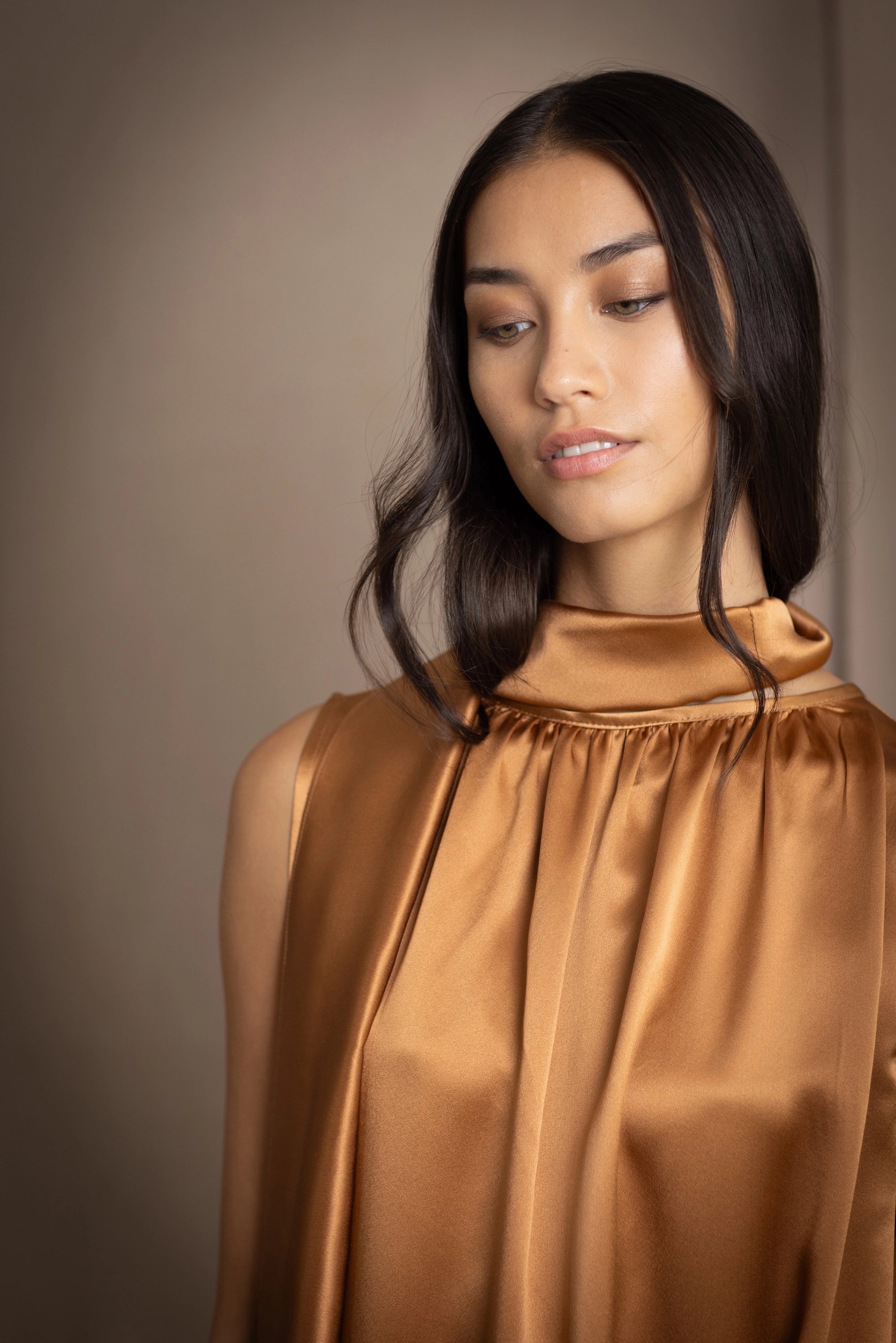 a woman wearing a bronze silk sleeveless dress