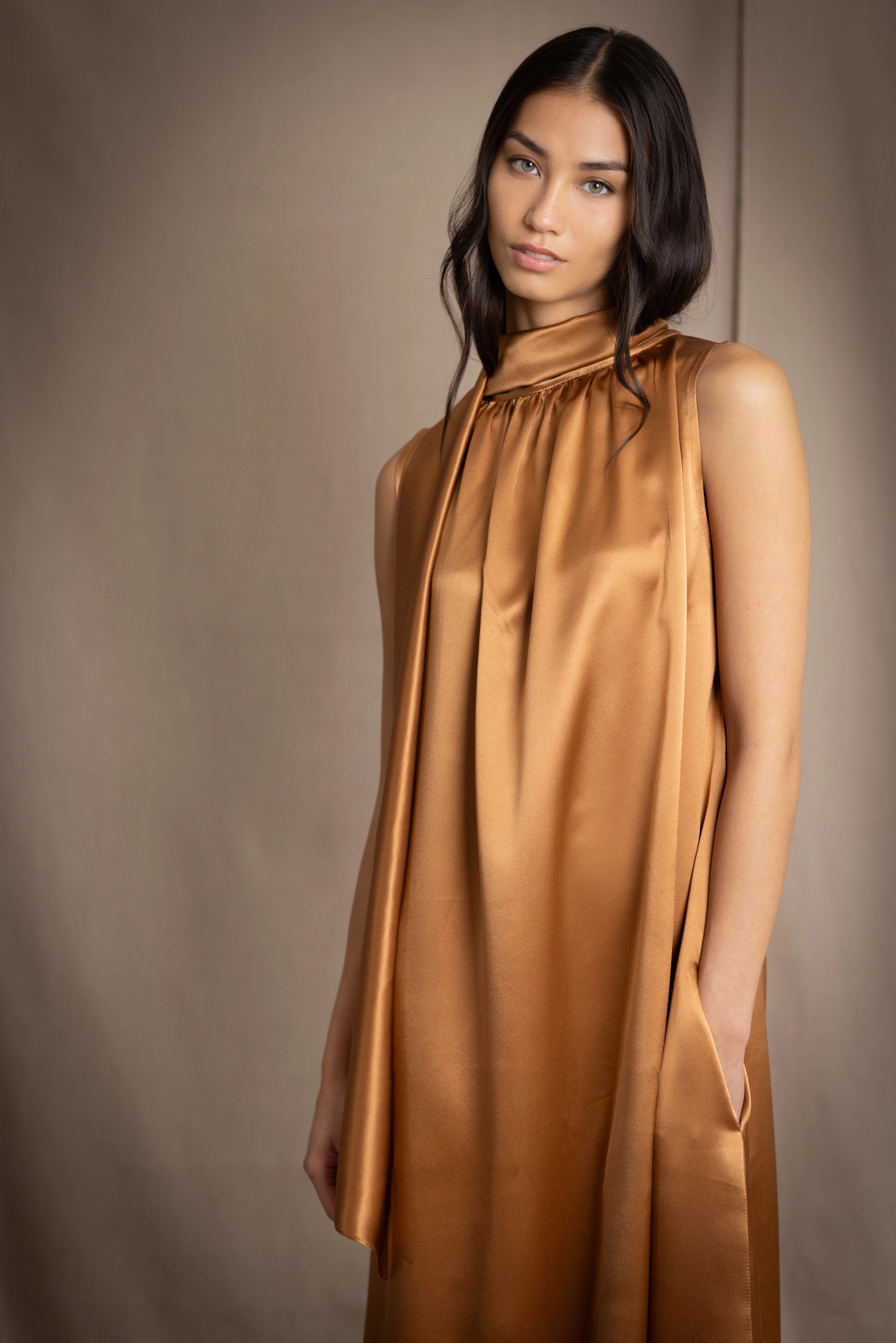 a woman wearing a bronze silk sleeveless dress