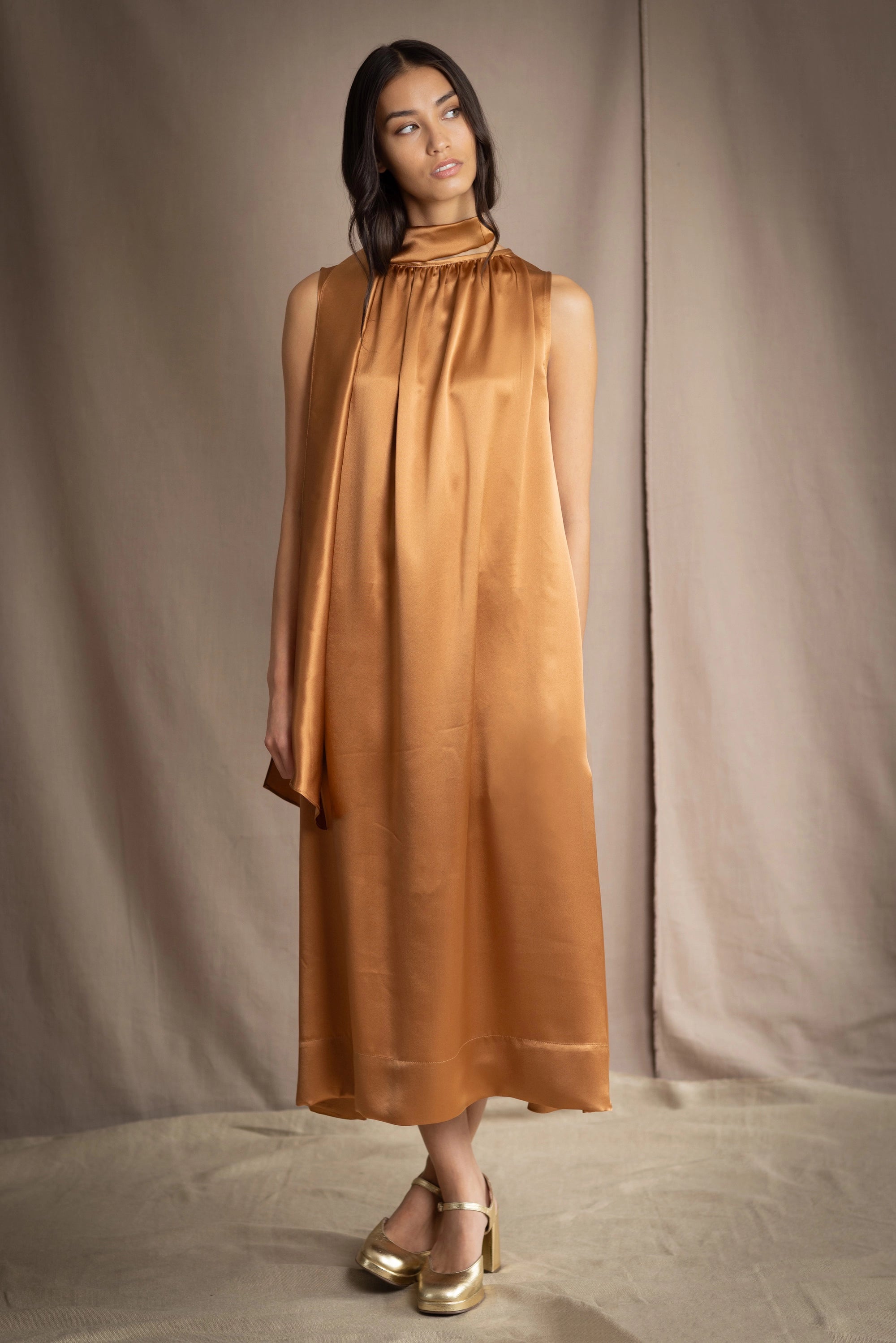 a woman wearing a bronze silk sleeveless dress