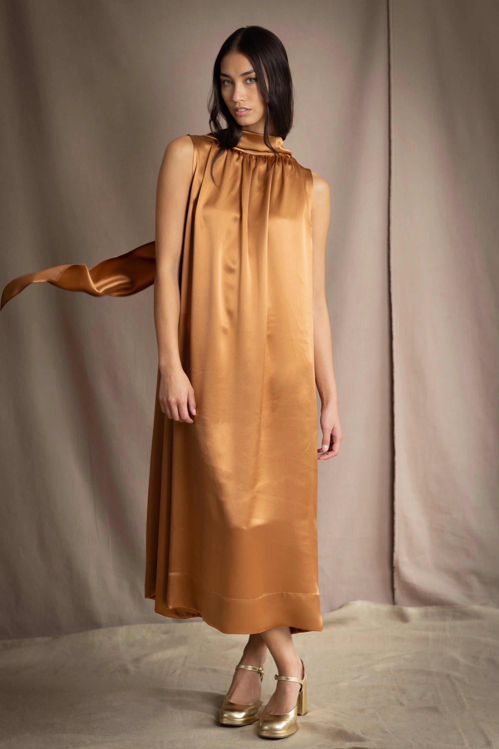a woman wearing a bronze silk sleeveless dress