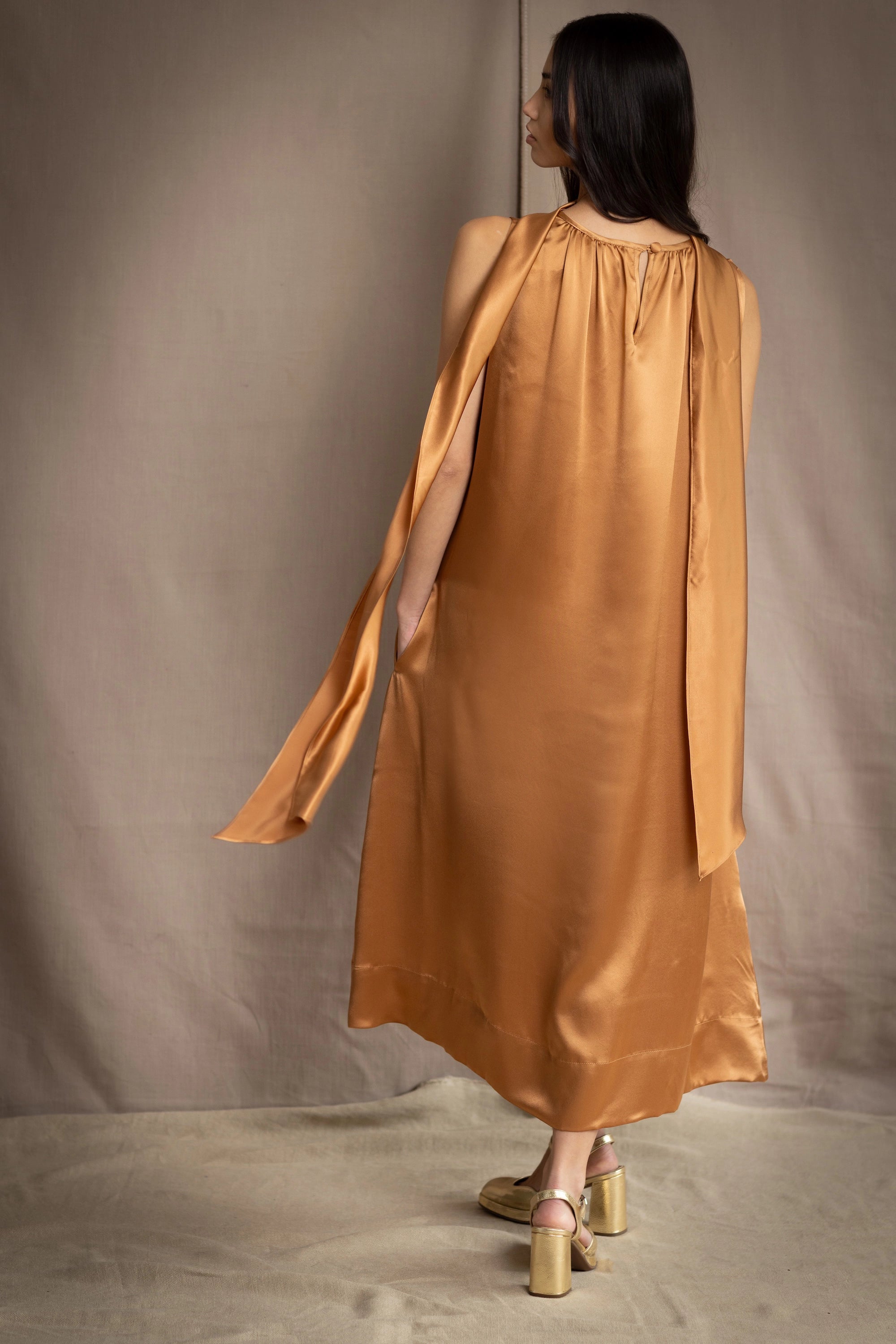 a woman wearing a bronze silk sleeveless dress