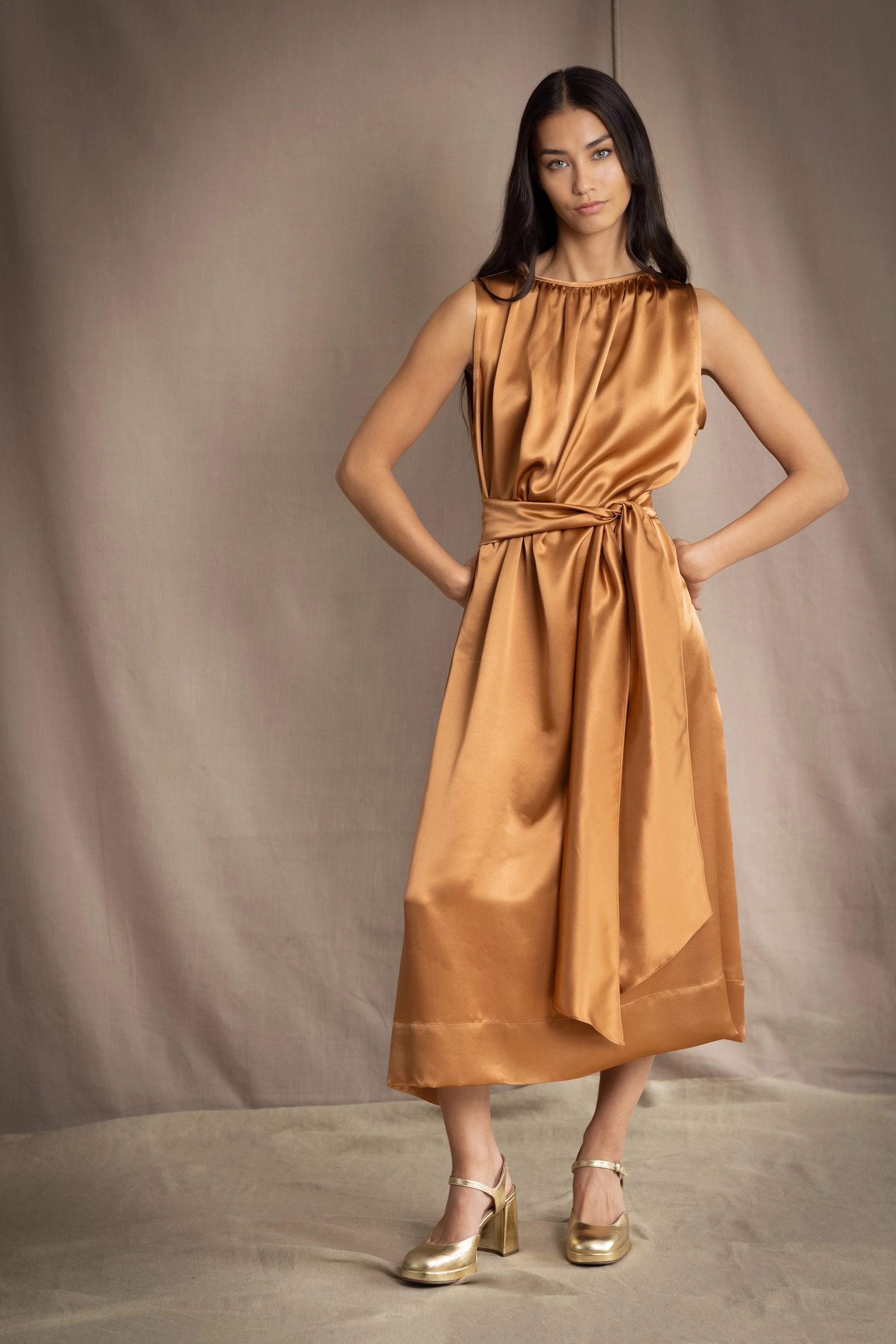 a woman wearing a bronze silk sleeveless dress