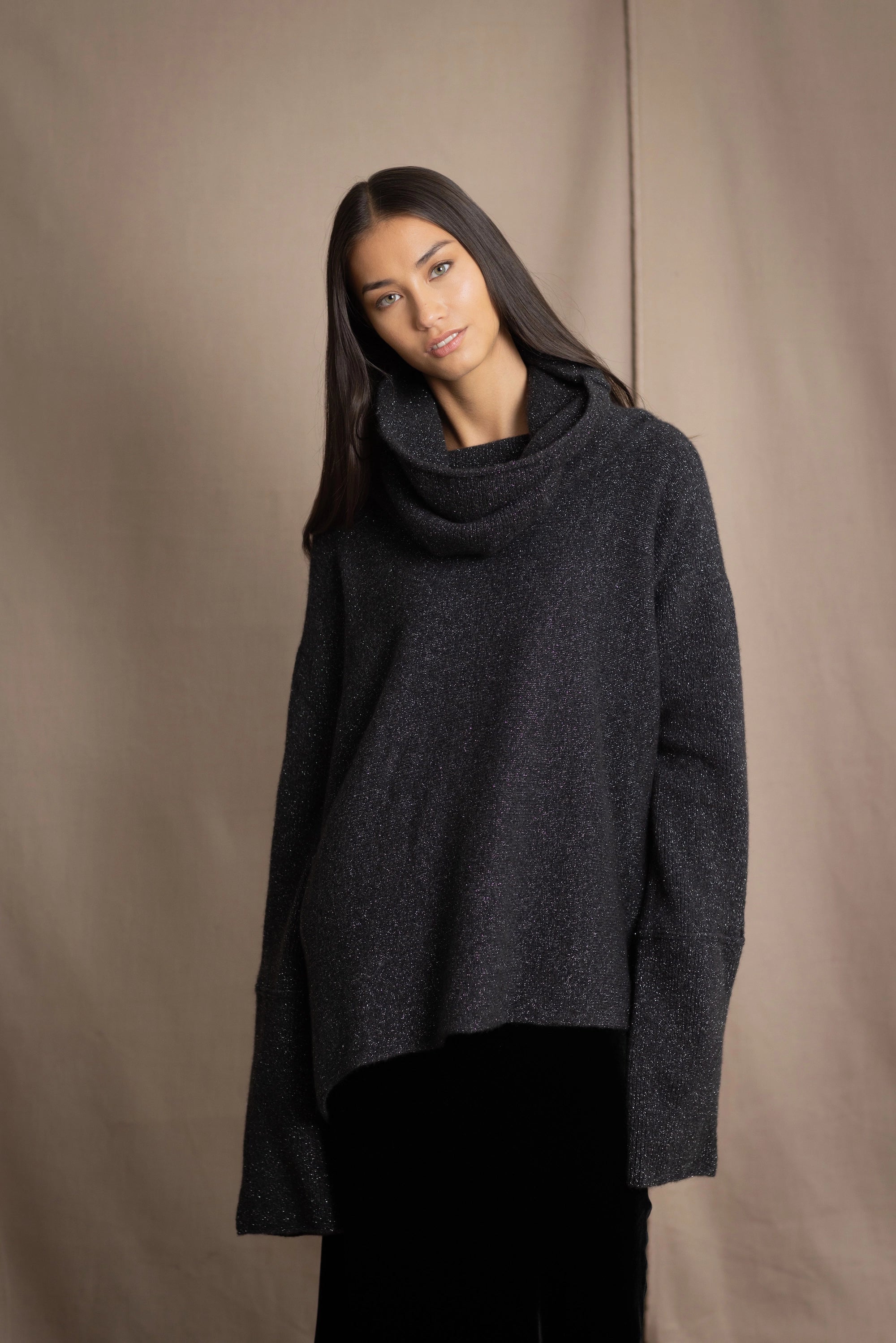 woman wearing an oversized cashmere sweater with cowl neck in black with silver metallic lurex thread over silk velvet skirt in black
