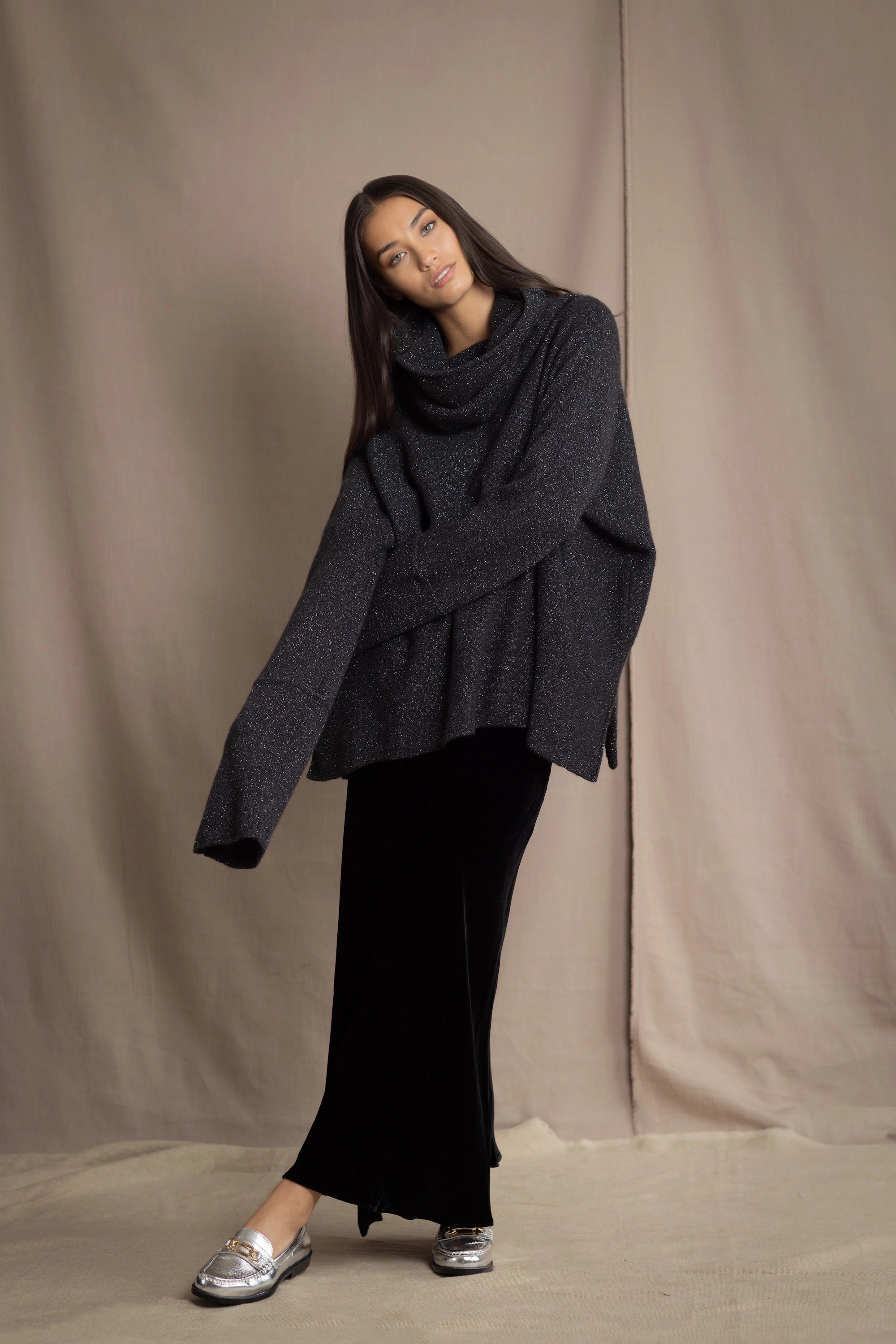 woman wearing an oversized cashmere sweater with cowl neck in black with silver metallic lurex thread over silk velvet skirt in black