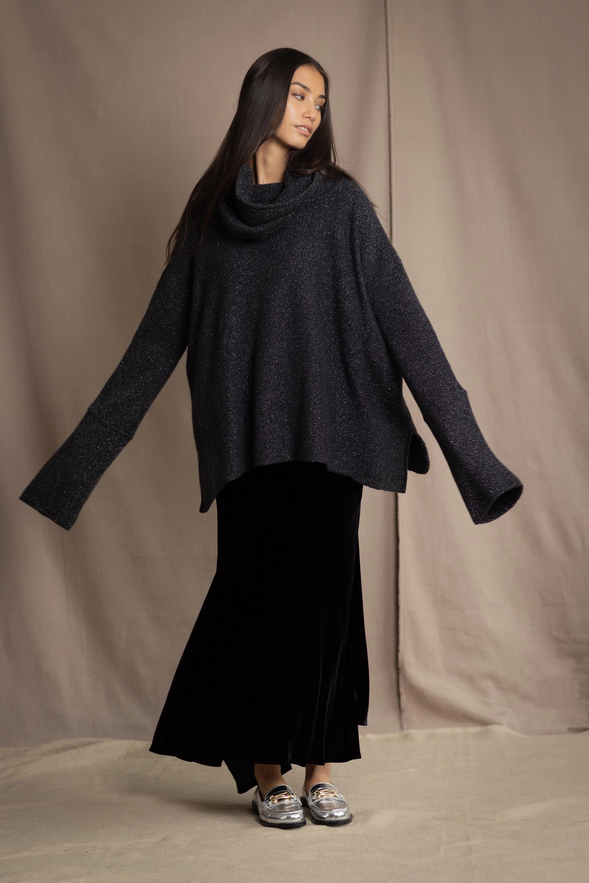 woman wearing an oversized cashmere sweater with cowl neck in black with silver metallic lurex thread over silk velvet skirt in black