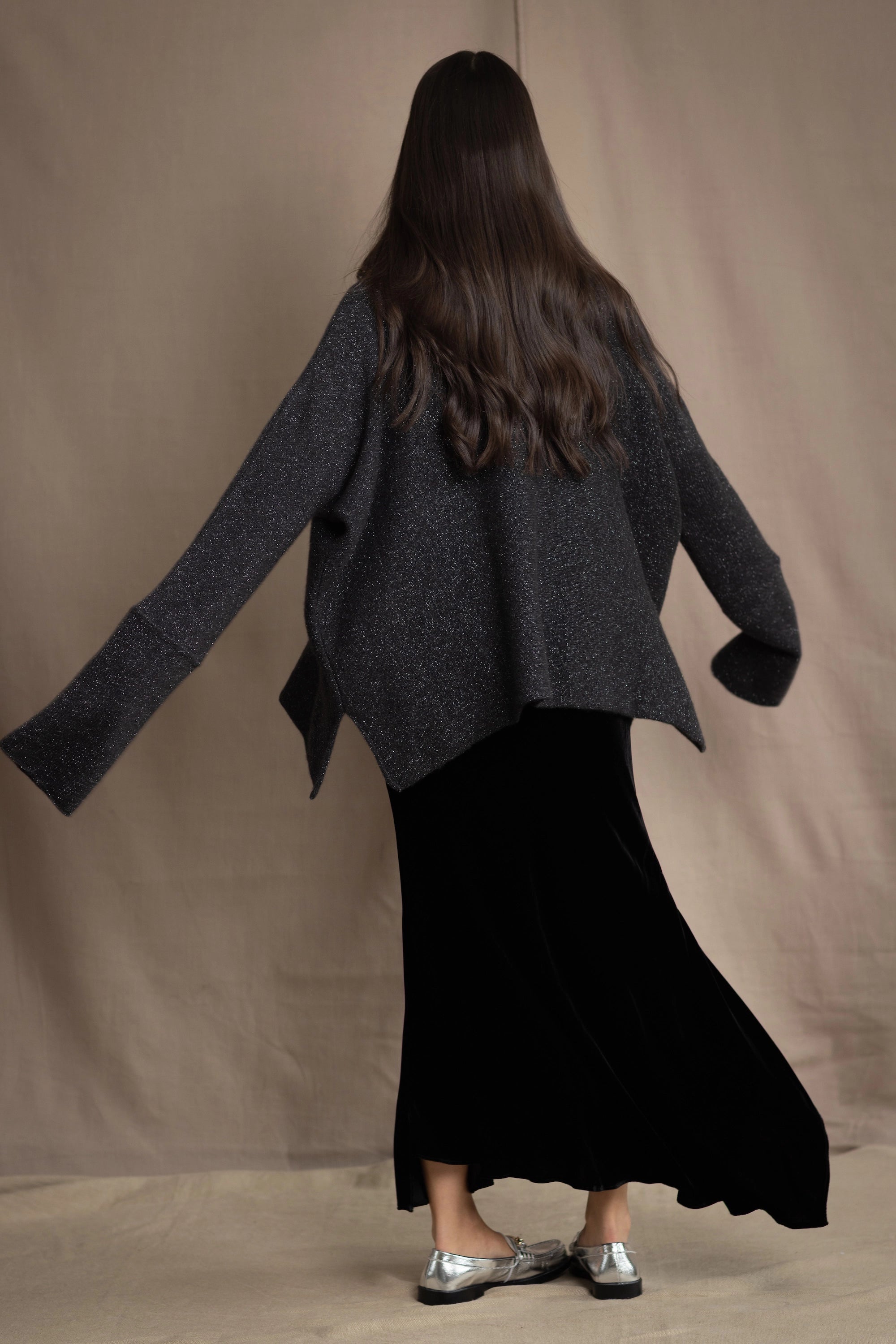 a woman wears a silk velvet skirt in black with black sparkly silver sweater on top