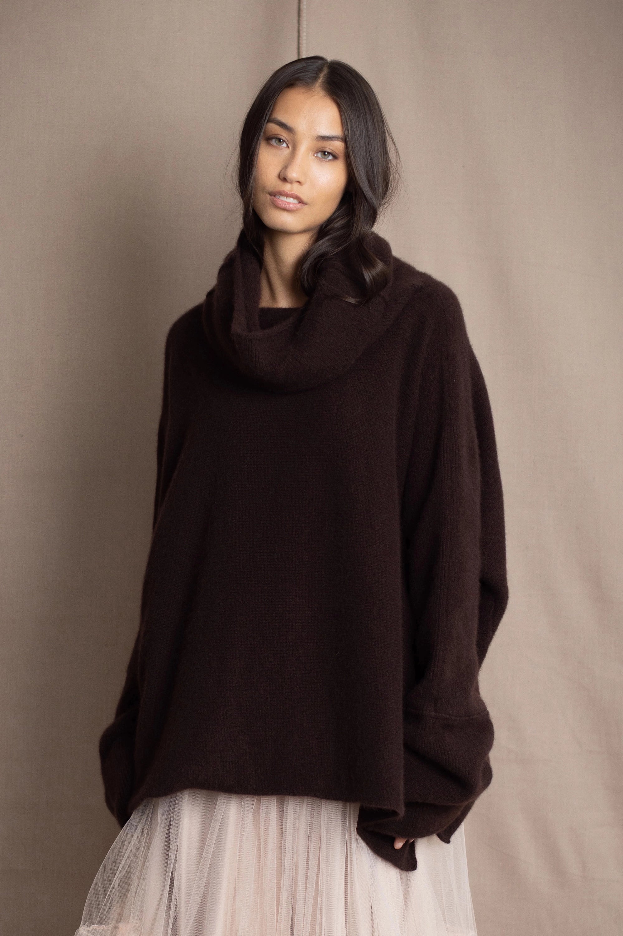 woman wearing an oversized cashmere sweater with cowl neck in dark brown over  pale pink tulle skirt