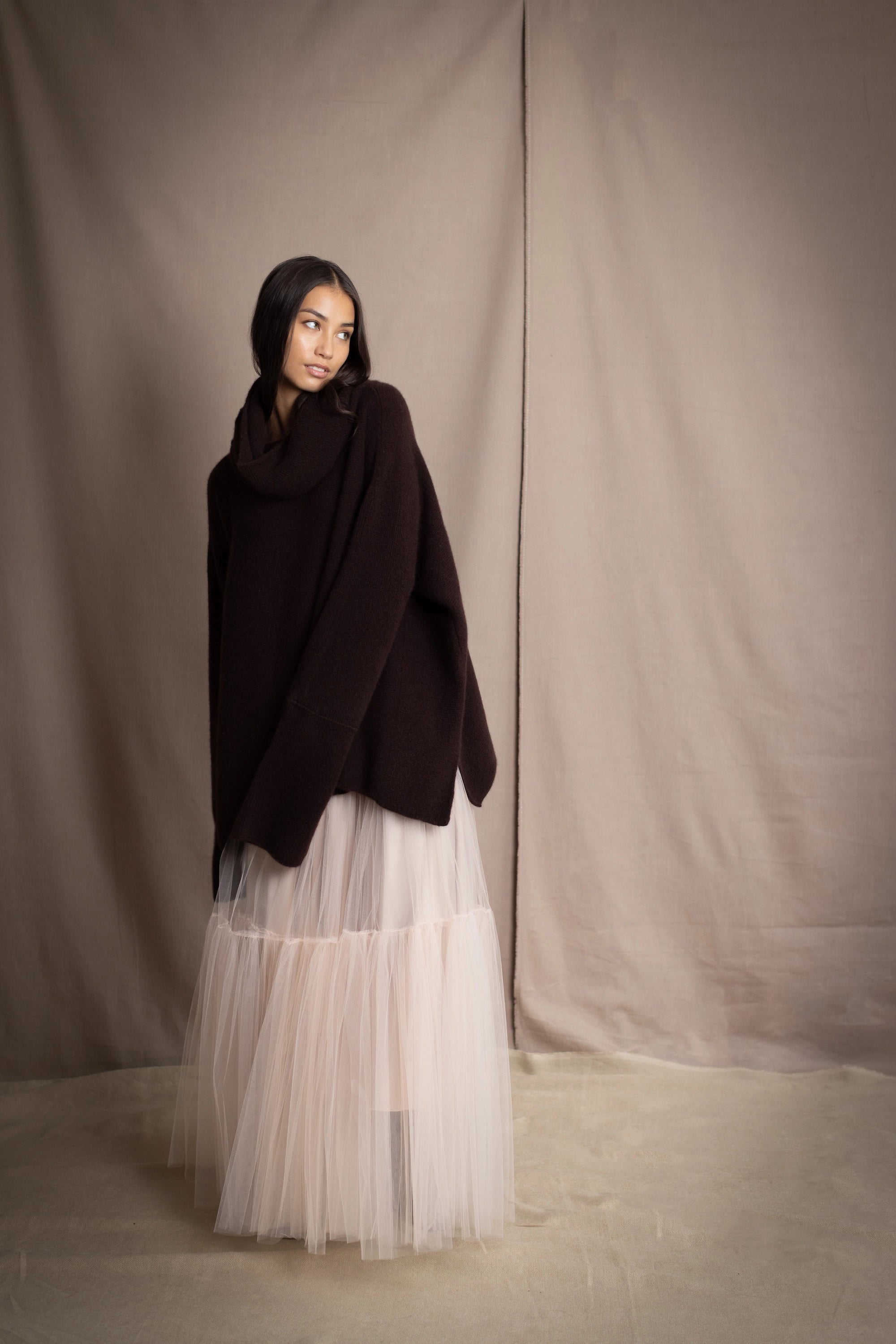 woman wearing an oversized cashmere sweater with cowl neck in dark brown over  pale pink tulle skirt