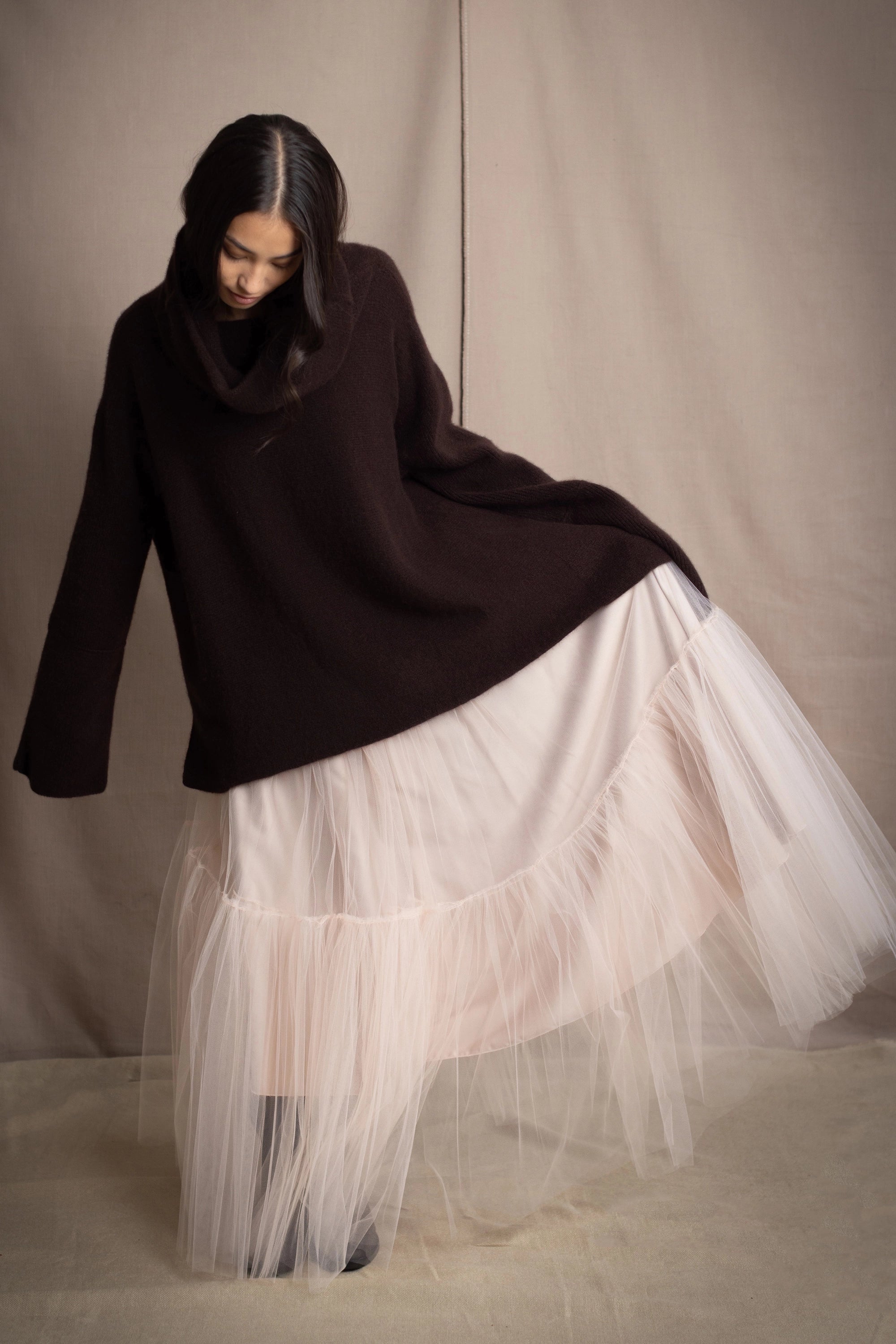 woman wearing an oversized cashmere sweater with cowl neck in dark brown over  pale pink tulle skirt