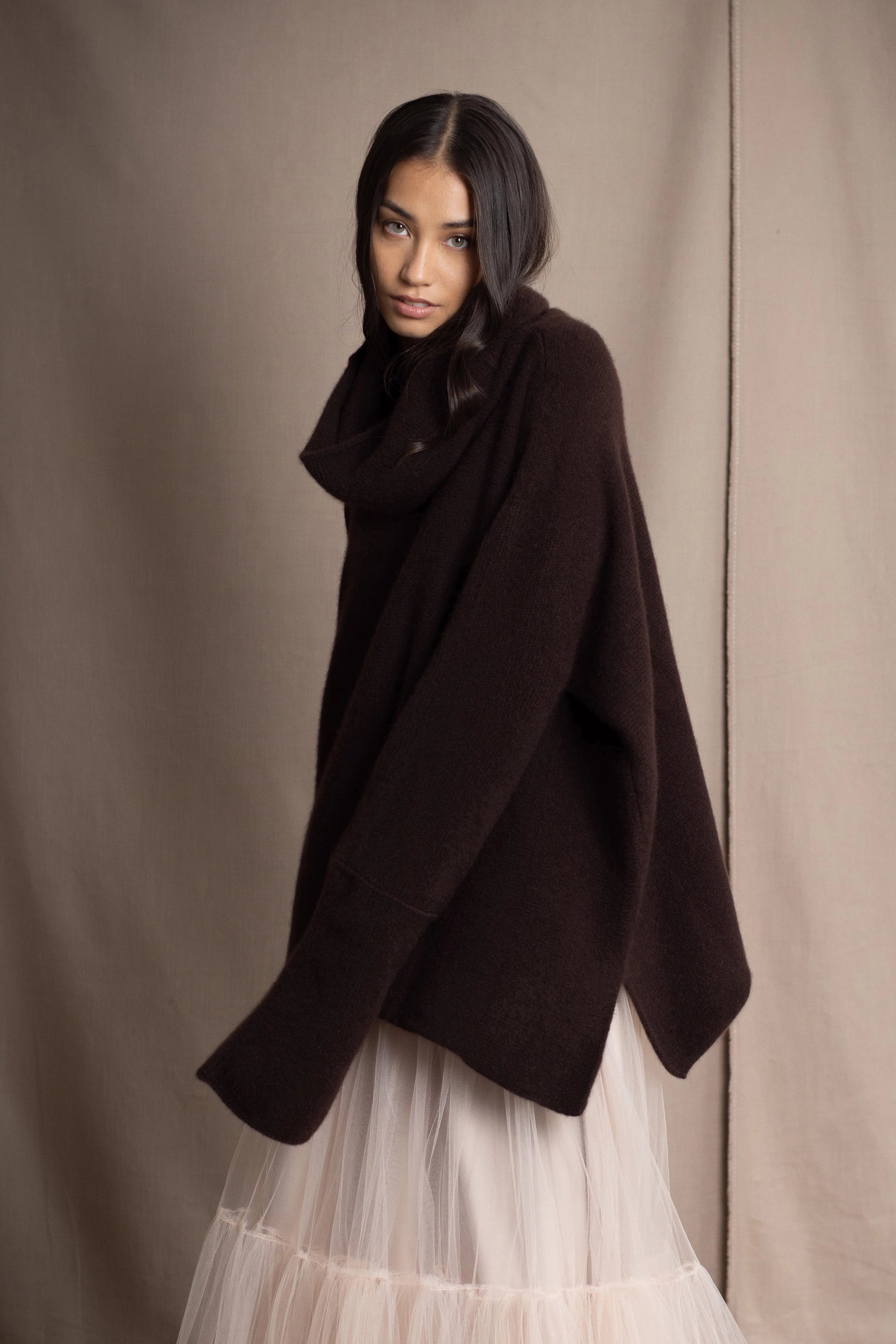 woman wearing an oversized cashmere sweater with cowl neck in dark brown over  pale pink tulle skirt