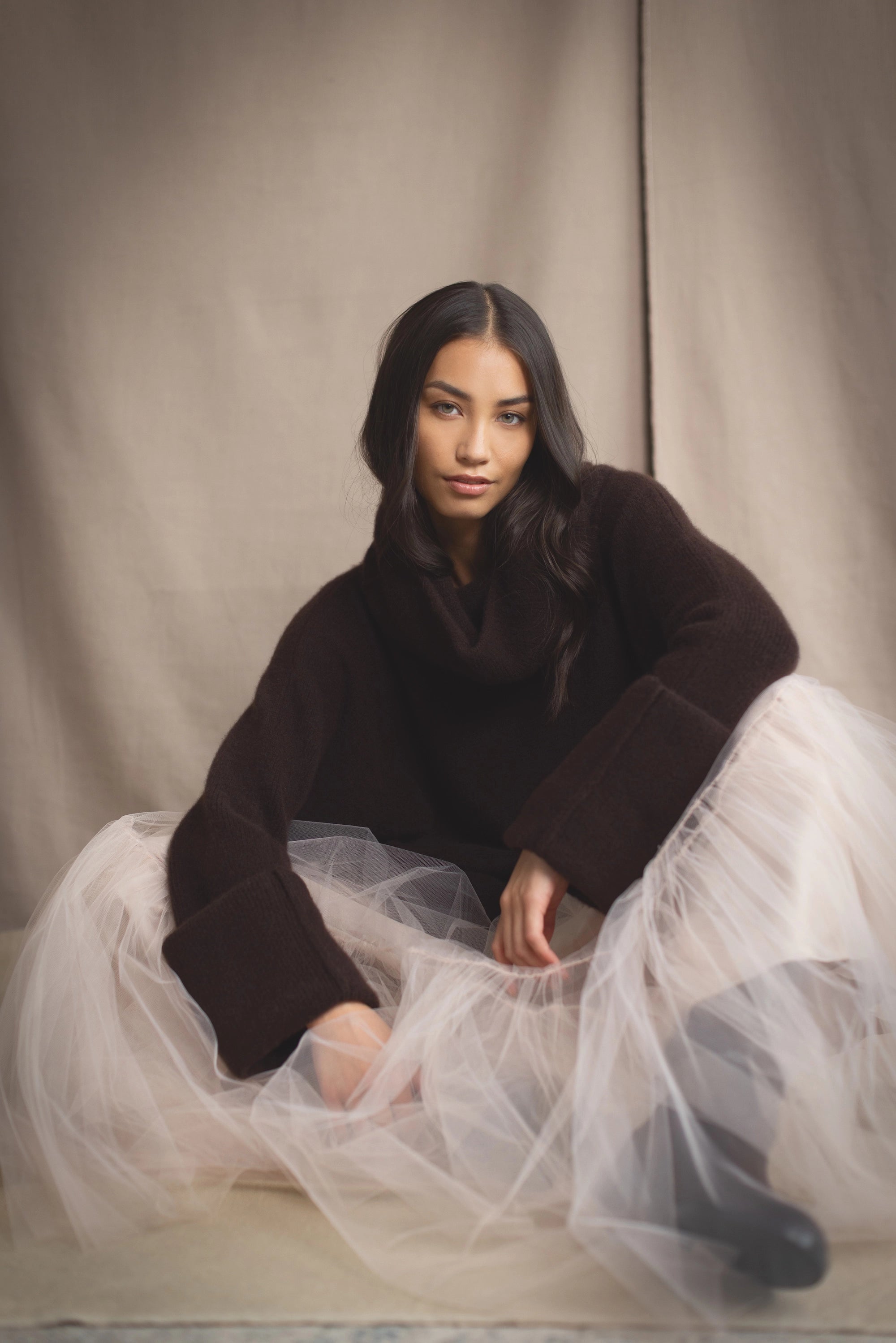 woman wearing an oversized cashmere sweater with cowl neck in dark brown over  pale pink tulle skirt