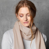 a lady wears a small cashmere scarf in a warm neutral beige colour