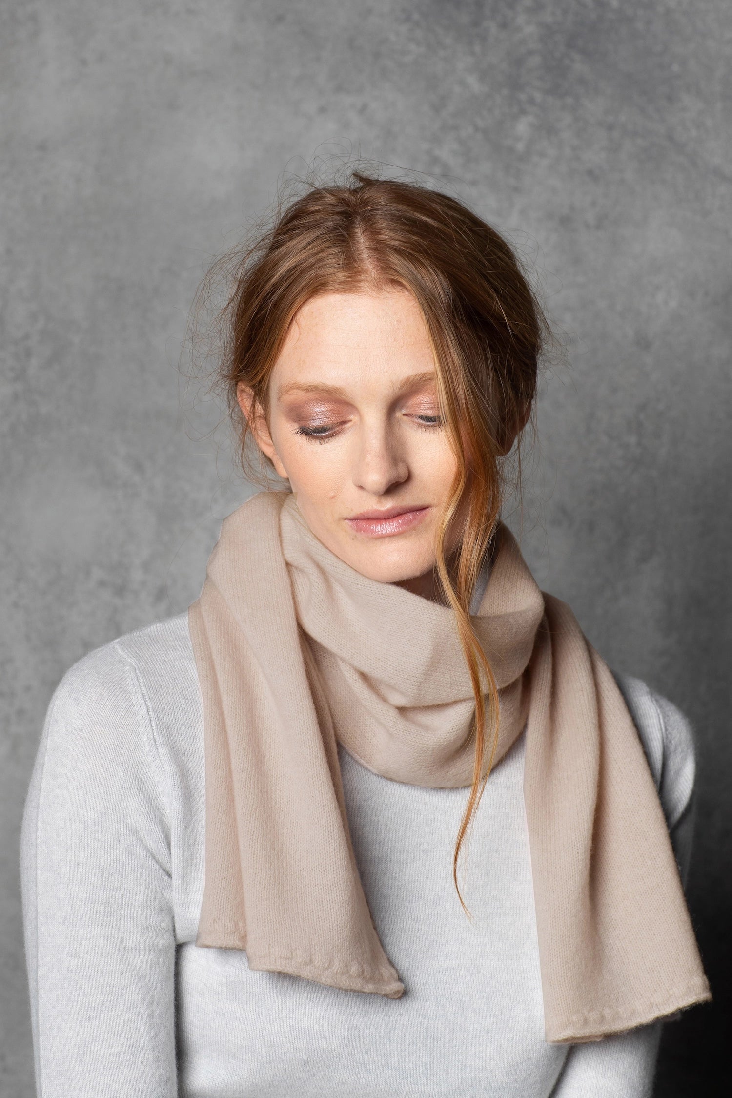 a lady wears a small cashmere scarf in a warm neutral beige colour