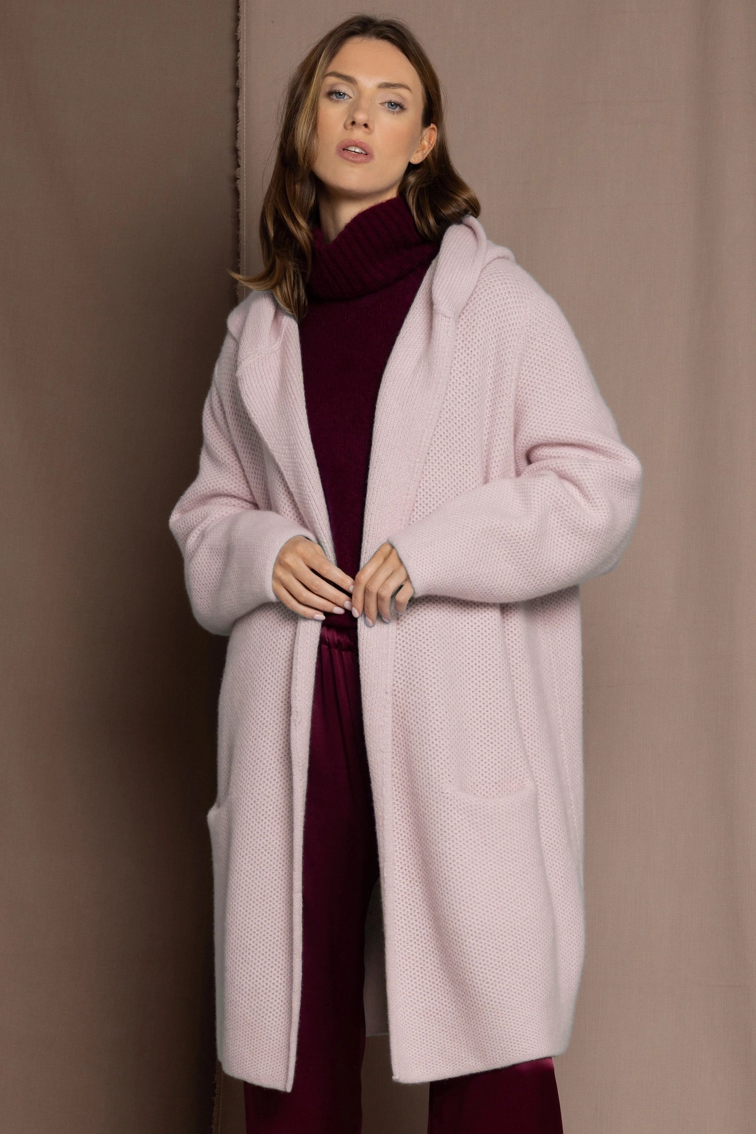 woman wearing a long cashmere coat cardigan in pale pink over burgundy cashmere sweater and burgundy silk trousers