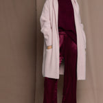 woman wearing a long cashmere coat cardigan in pale pink over burgundy cashmere sweater and burgundy silk trousers