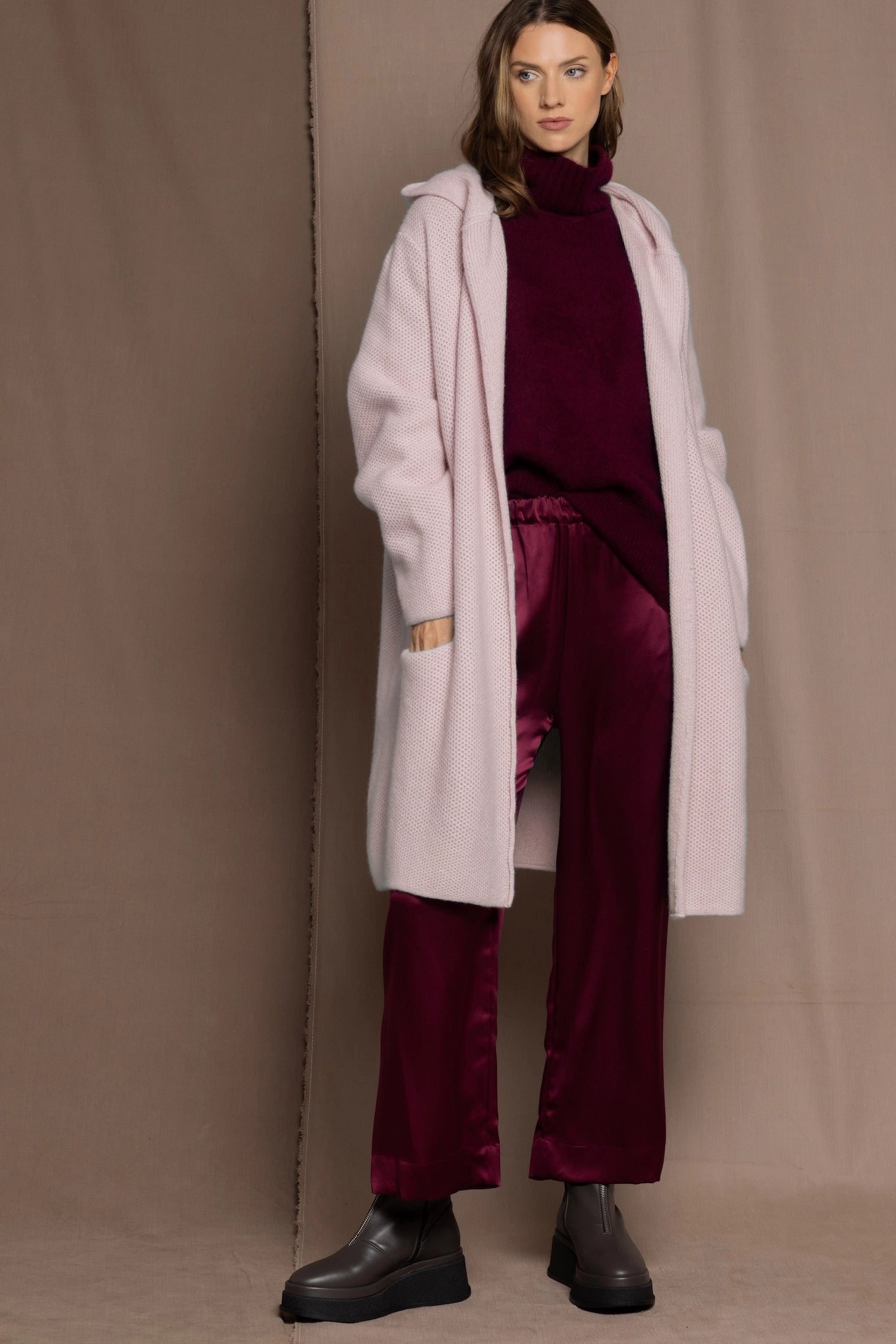 woman wearing a long cashmere coat cardigan in pale pink over burgundy cashmere sweater and burgundy silk trousers