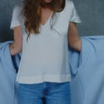A woman wears a 100% silk v-neck t-shirt in white and 100% cashmere coat in pale blue with a pair of jeans