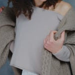 A woman wears a cropped cashmere sweater in beige with white silk shorts and a large cashmere aran blanket throw in taupe