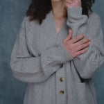 a woman wears a traditional irish aran cardigan sweater made from pure 100% cashmere in taupe