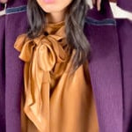 video of a woman wearing a long purple cashmere coat, bronze silk blouse and silk pants with dark purple cashmere beanie hat