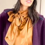 video of a woman wearing a cashmere beanie hat in dark purple with cashmere coat in dark purple and bronze silk pussy bow top