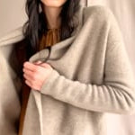 video of a woman wearing a beige cashmere cardigan with gold metallic lurex thread over a bronze silk dress