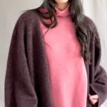 video of a woman wearing a long brown cashmere coat, pink cashmere sweater, blue jeans, and pink cashmere beanie